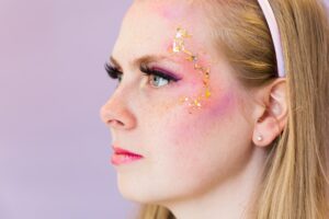 Mulher loira com maquiagem rosa e brilho, de perfil